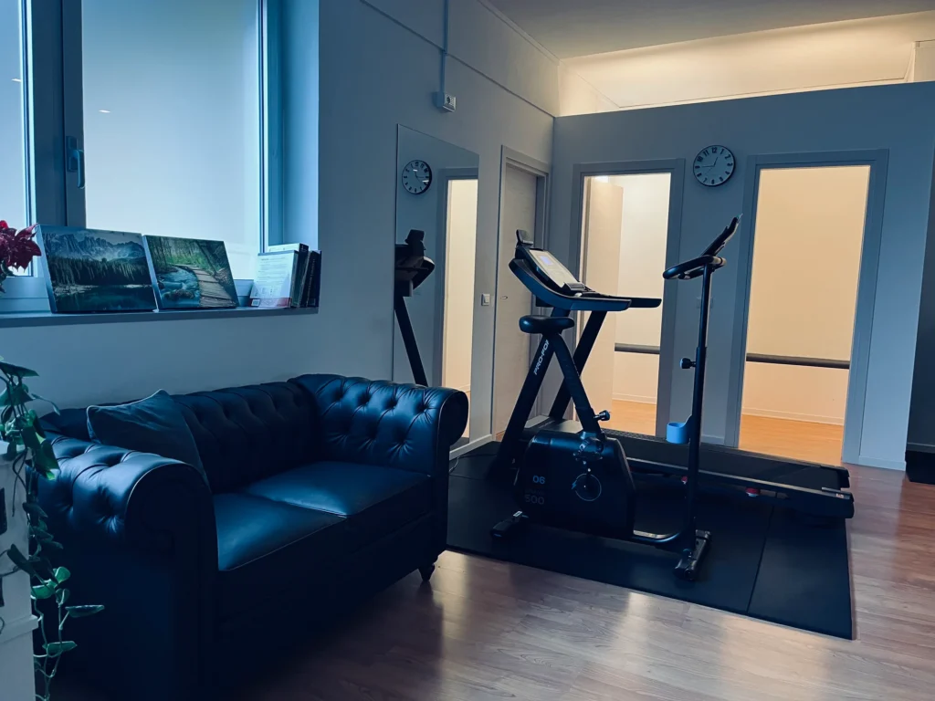 Sala clinica moderna con divano in pelle, cyclette e pareti a specchio.
